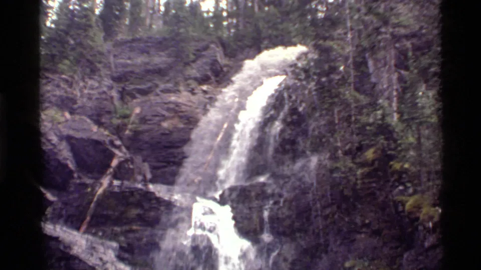 Water pours over a forested rock ledge in this 1972 Holland Lake, Montana home-movie frame.