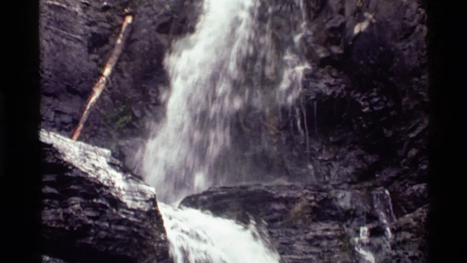 Close 1972 8mm view of the Montana waterfall as frothy water drops through a narrow rocky channel.