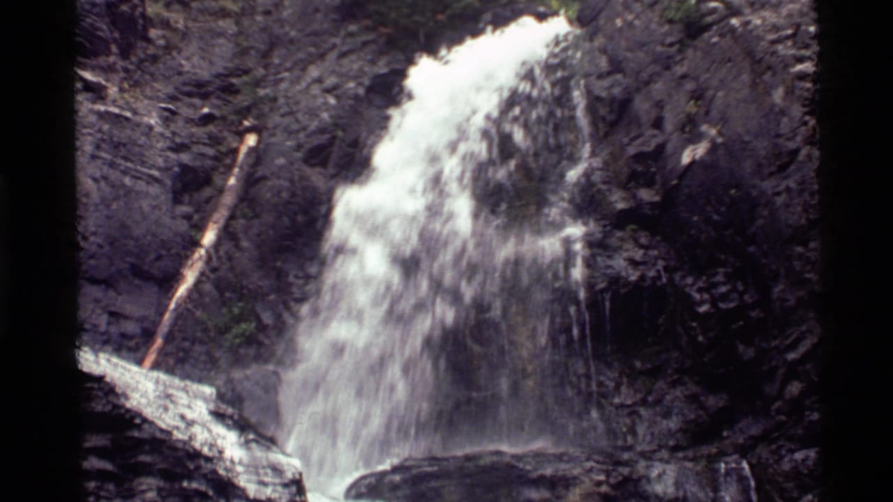 Waterfall dropping over dark rock with a fallen log near the left side.
