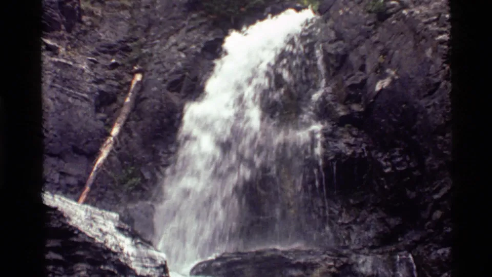 1972 8mm view at Holland Lake, Montana, showing white water pouring over dark rock beside a fallen log.