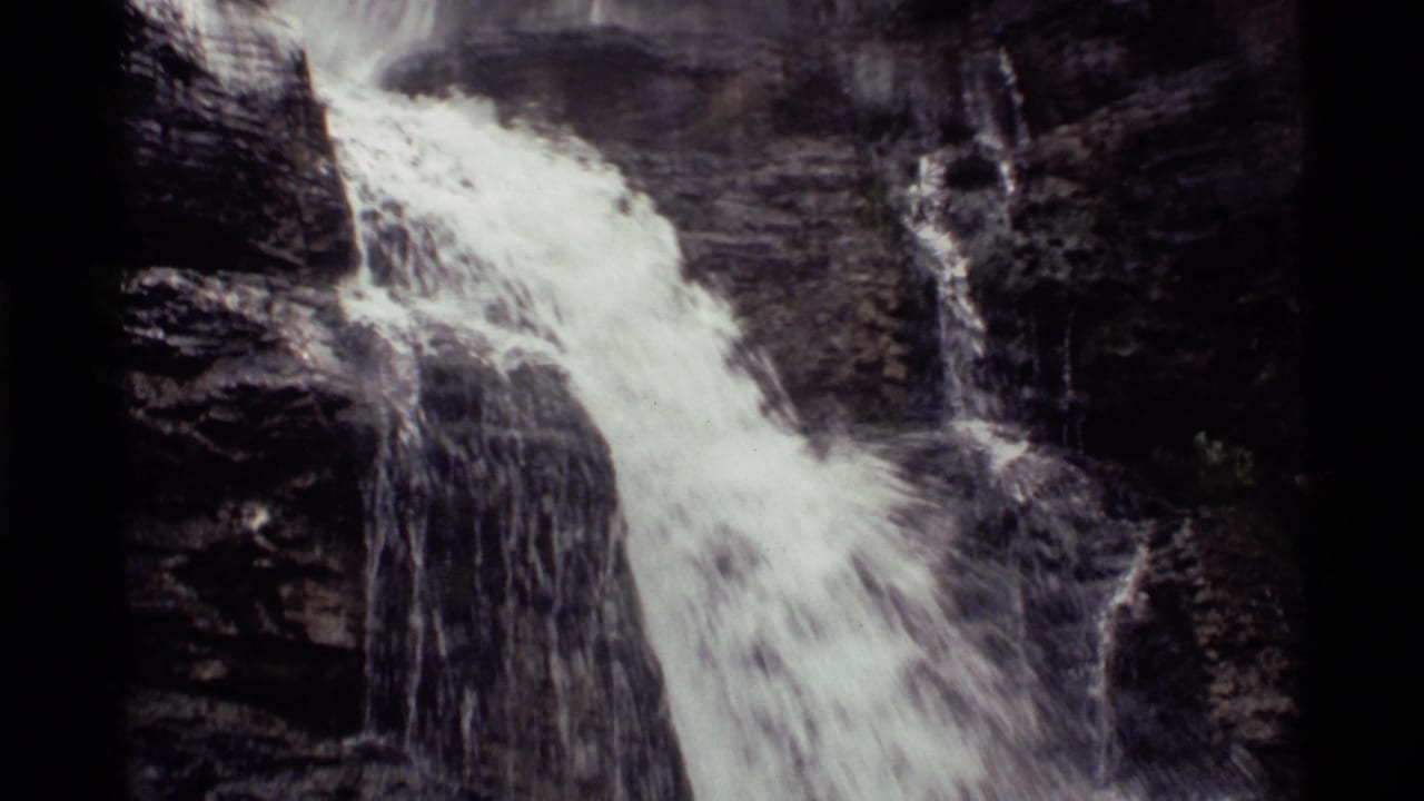 1972 Holland Lake, Montana home-movie frame showing water cascading diagonally over dark rock ledges.