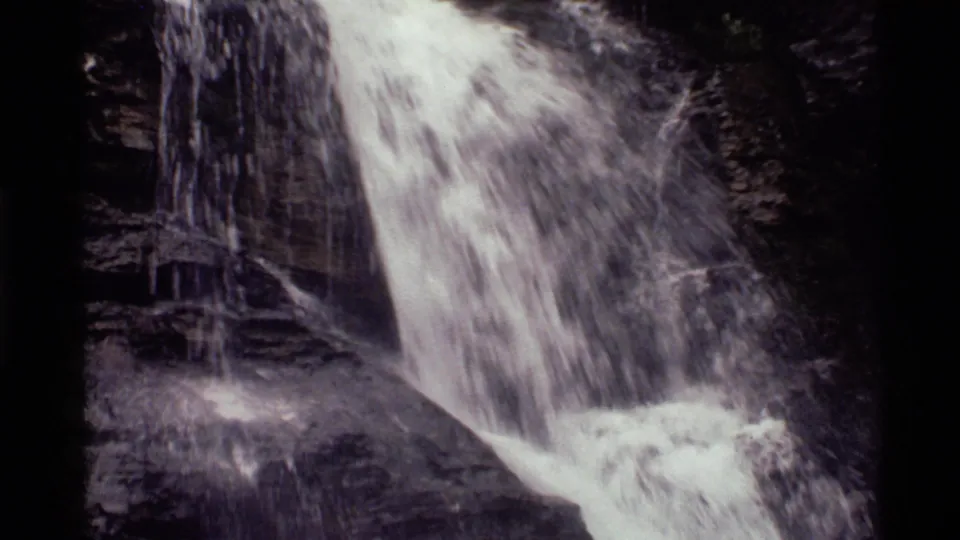 1972 Montana waterfall frame with rushing water, layered cliff stone and visible 8mm grain.