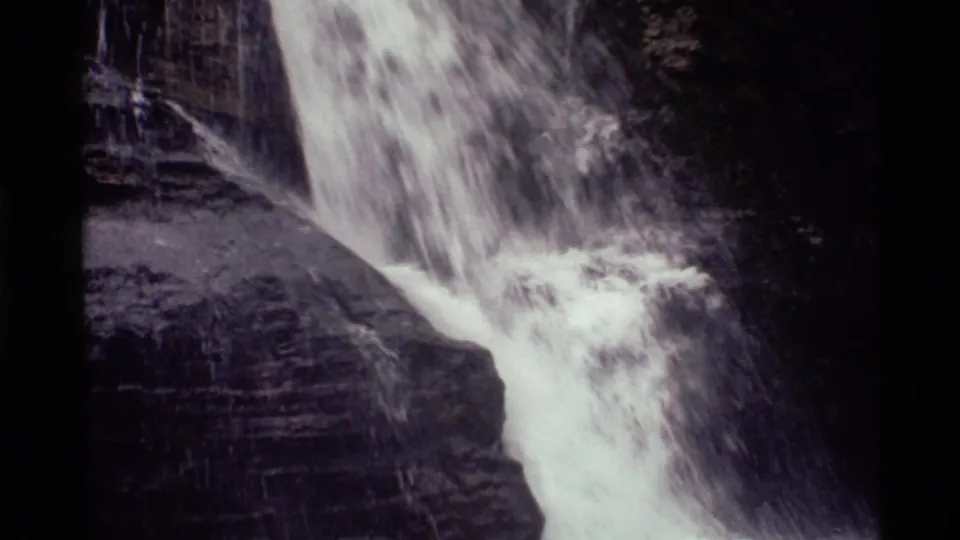 Holland Lake waterfall seen in black-and-white home-movie footage, with water breaking over stepped rock.