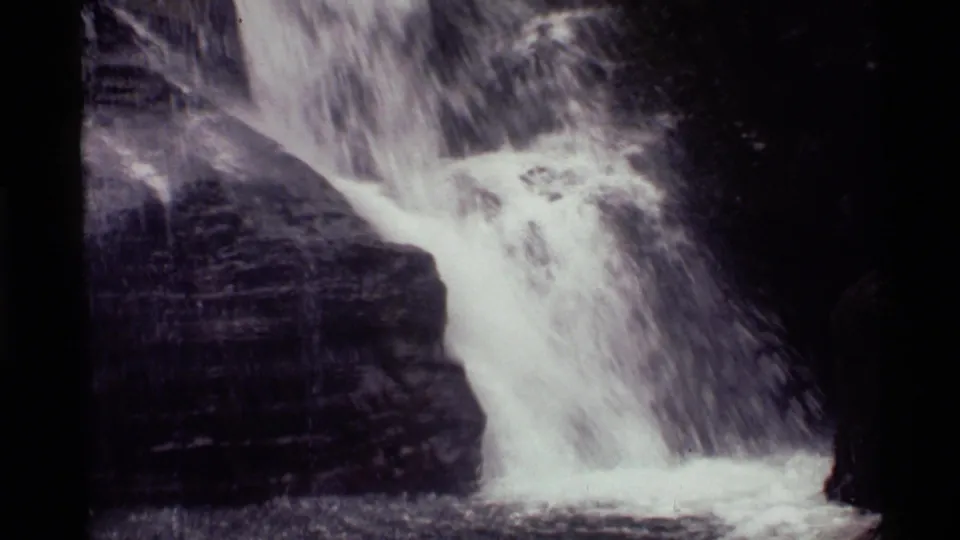 1972 8mm frame from Holland Lake, Montana, showing white water cascading over dark layered rock.