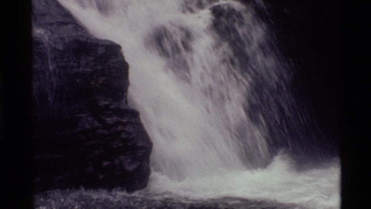 Close view of a waterfall pouring past a dark rock wall.