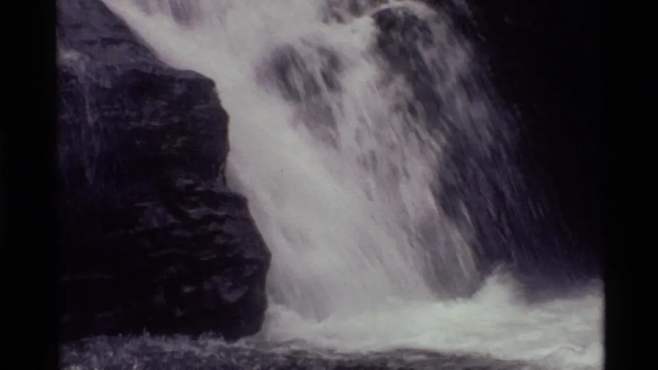 1972 Holland Lake 8mm still with rushing water sliding past a dark rock formation into foam.