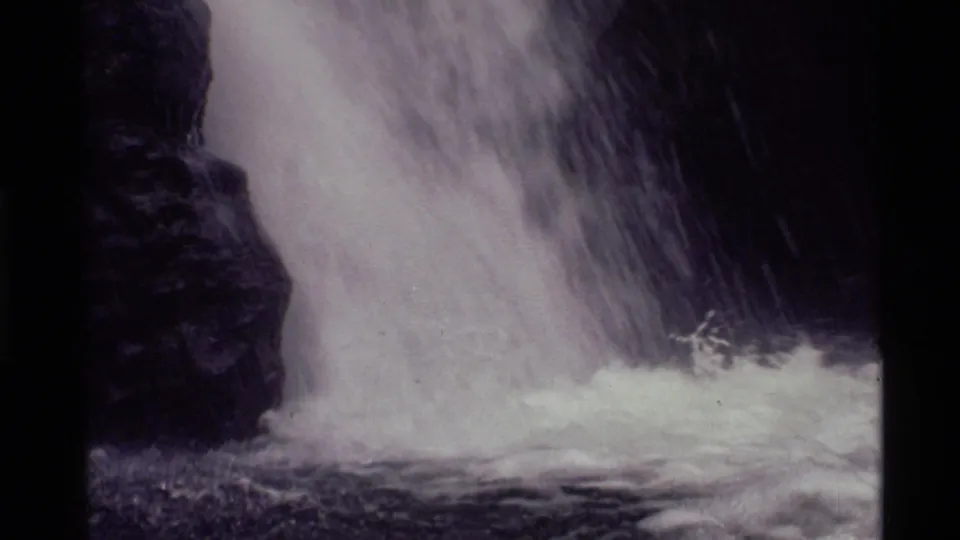 1972 Holland Lake home-movie still showing the cascade crashing into a frothy pool by dark rock.