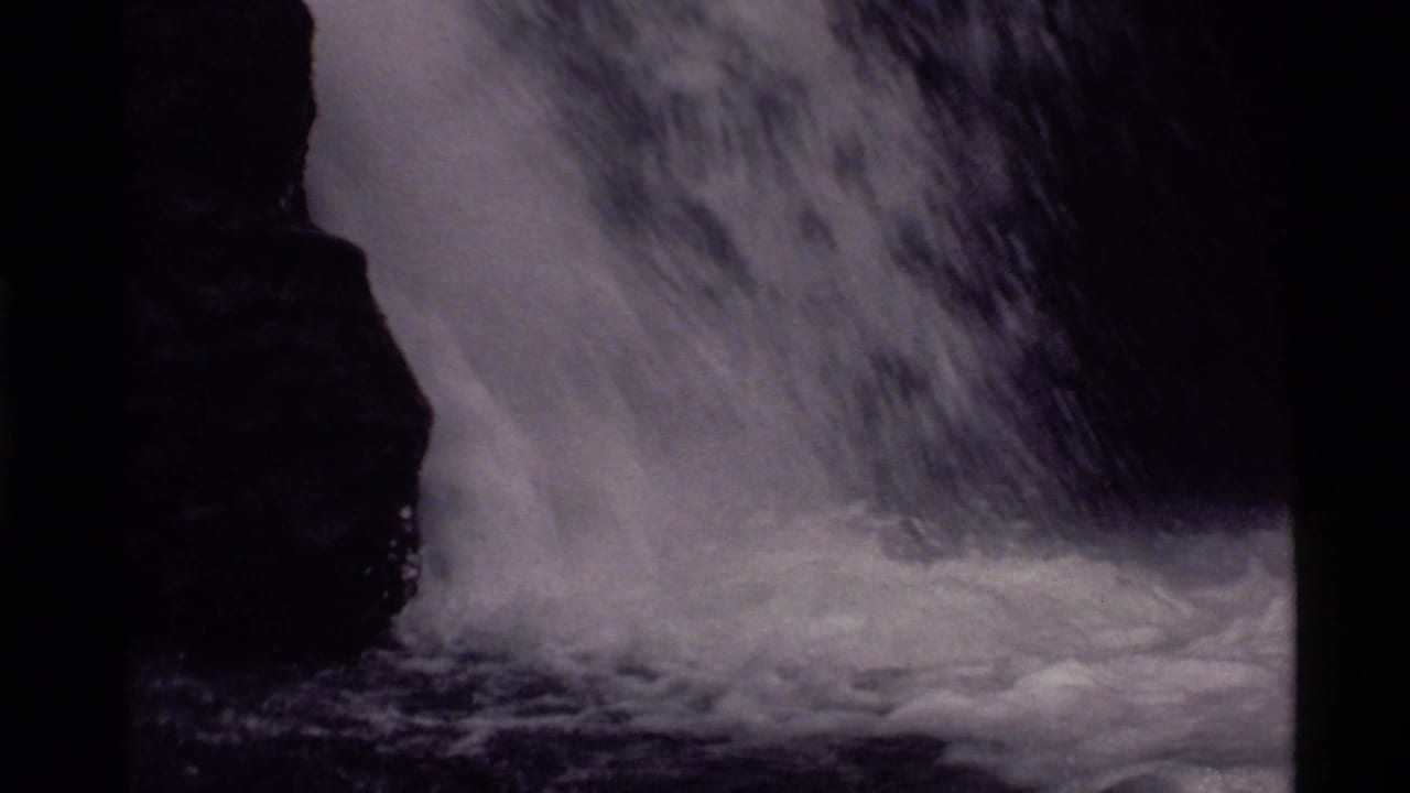 1972 8mm frame from Holland Lake, Montana showing turbulent water falling beside dark mountainside rock.