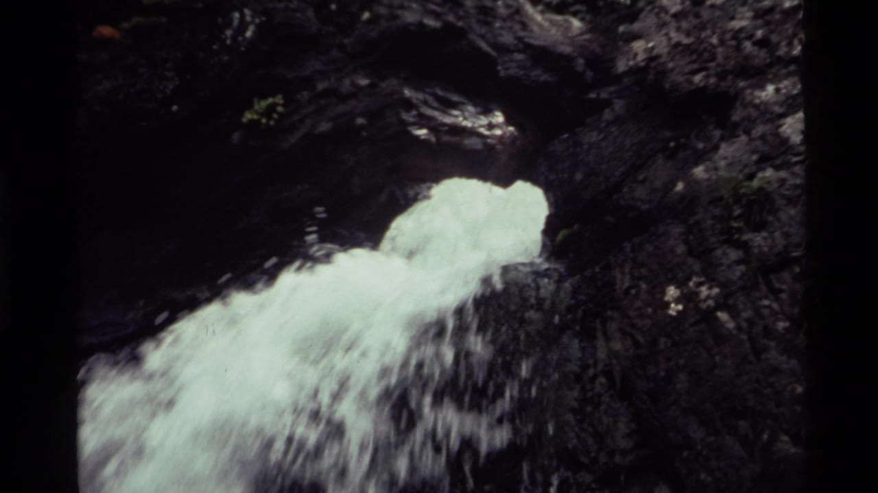 1972 8mm Holland Lake footage shows frothy white water spilling over dark, rugged rock near the upper part of a waterfall.