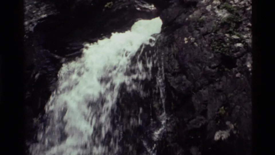 1972 Holland Lake 8mm frame with white water dropping from a rocky ledge into a shadowed chute between dark stone walls.