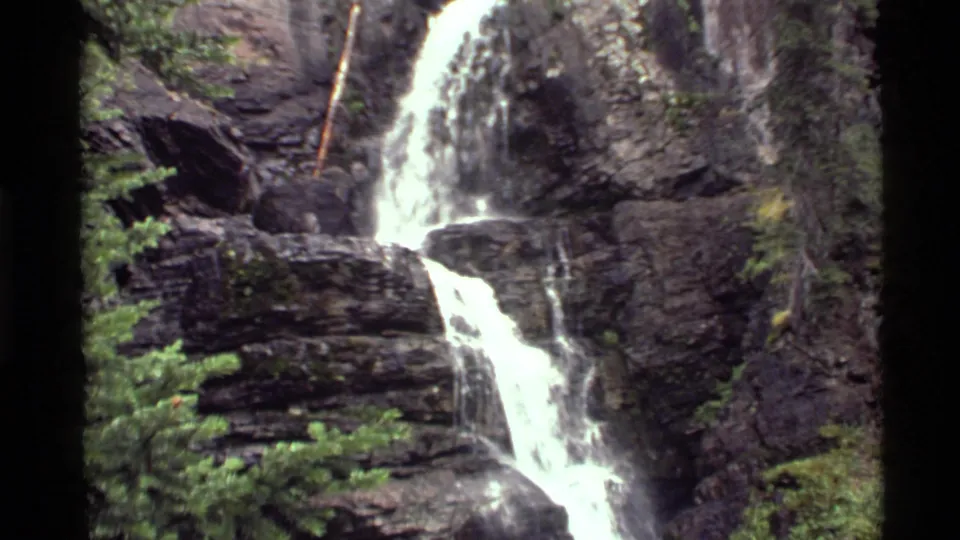 1972 8mm view of the Holland Lake waterfall widening to include foreground foliage, cliff rock, and the bright lower flow.