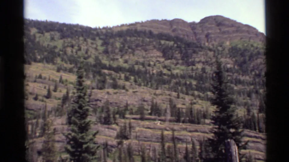 1972 Holland Lake, Montana frame showing rocky ridges, scattered pine growth, and a dark central film-frame divider.