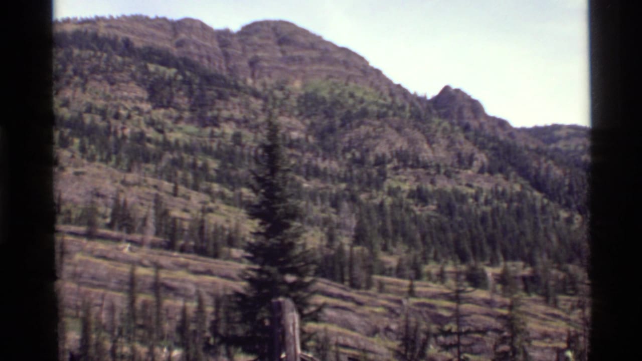 Similar mountain view with trees, rocky ridges, and visible film gate edges.