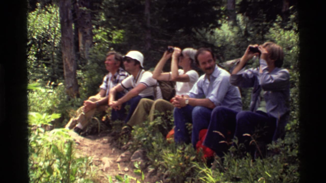 Five hikers rest on a forest trail while two look through binoculars.