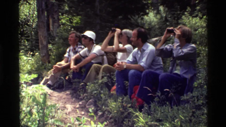 A 1972 home-movie frame shows the hikers resting together on the trail, surrounded by dense trees and undergrowth.