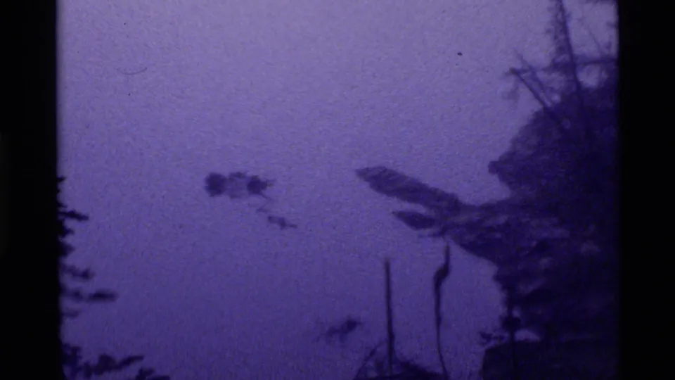 1972 Holland Lake 8mm frame showing calm purple water, a small dark floating object, and dark evergreen silhouettes along the right side.