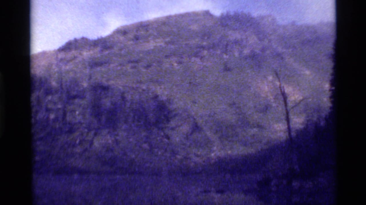 1972 Holland Lake, Montana footage showing a rocky, tree-covered mountain slope under a pale sky with soft 8mm grain.