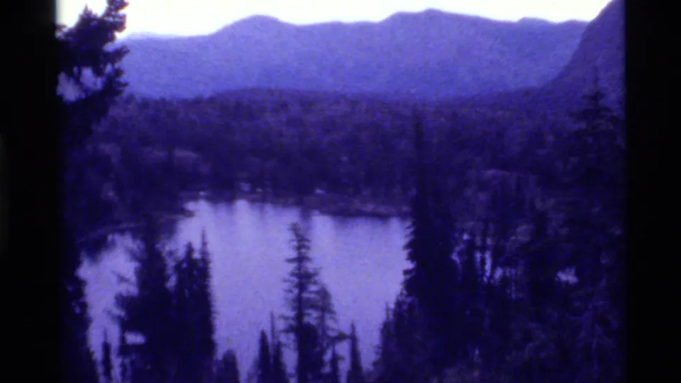 1972 8mm scenic view of Holland Lake in Montana, showing water, pine forest, mountain ridges, and dark small-gauge film edges.