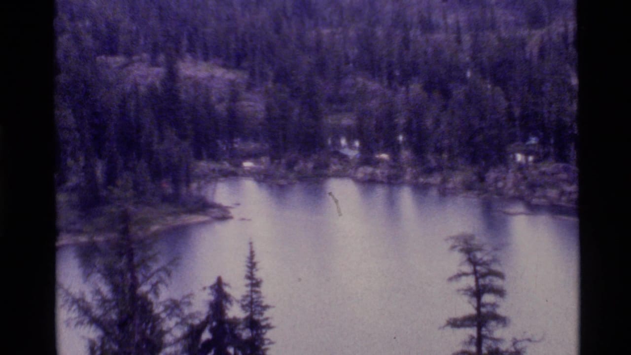 1972 Holland Lake, Montana home-movie frame showing still water, forested shoreline, and dark 8mm scan borders.