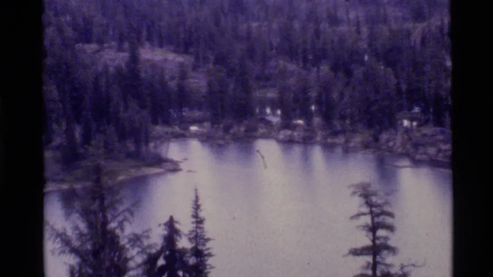 1972 Holland Lake, Montana home-movie frame showing still water, forested shoreline, and dark 8mm scan borders.
