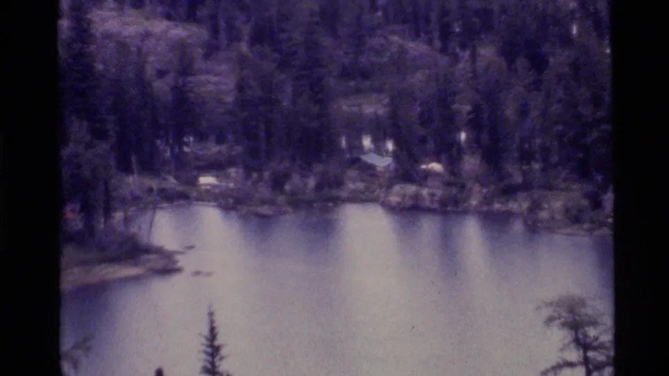 1972 Holland Lake, Montana frame with calm water, evergreen shoreline, and a soft purple 8mm color cast.