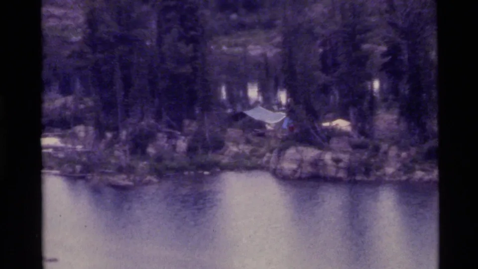 1972 Holland Lake, Montana frame showing a small tent or tarp near rocks and trees along the lakeshore.