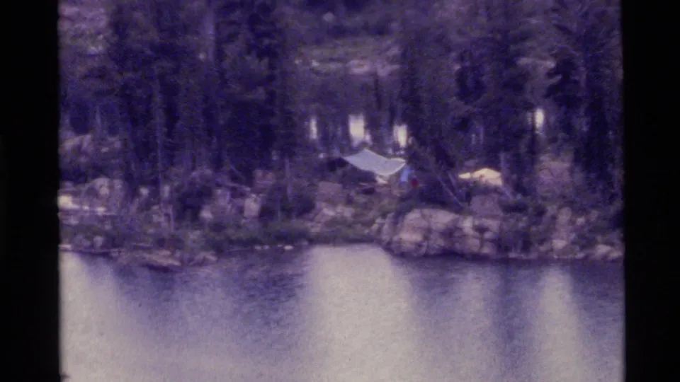 1972 Holland Lake, Montana home-movie frame of a tent and camp area tucked into trees above the waterline.