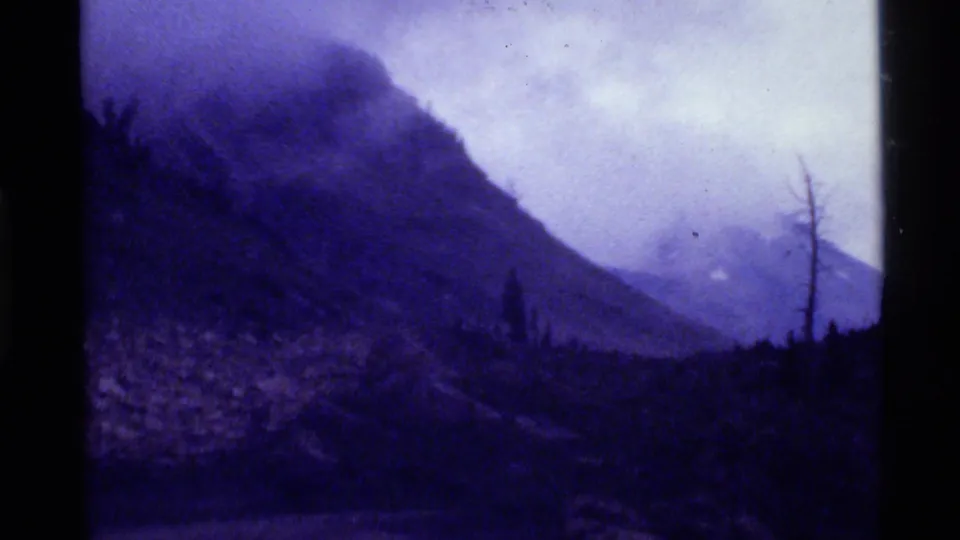 Purple-tinged 1972 8mm view of a Holland Lake mountain slope under haze or smoke, with dark foreground trees.