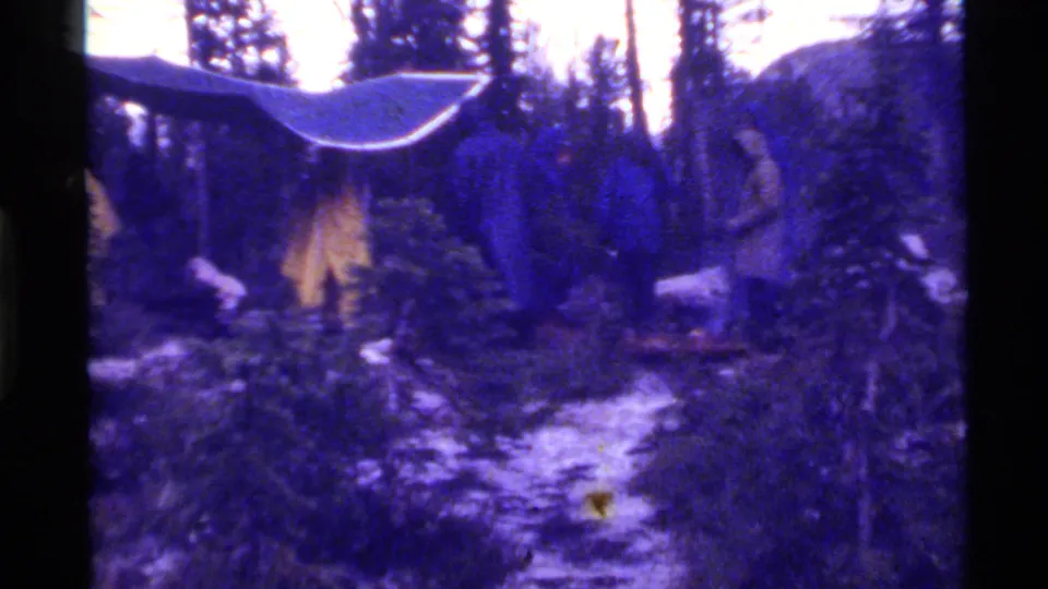 Purple-blue 8mm frame showing the Holland Lake campsite, tarp shelter, yellow tent, trees, rocky ground, and a partial figure at left.