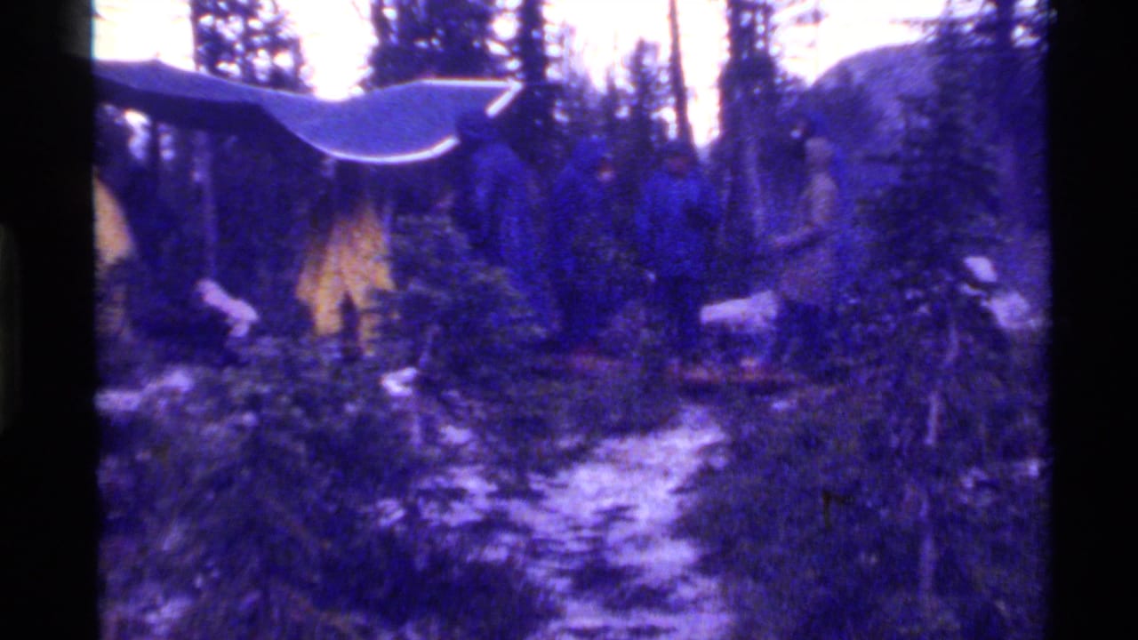 1972 Holland Lake, Montana 8mm frame showing a snowy evergreen forest with a small roofline or wooden structure partly visible.