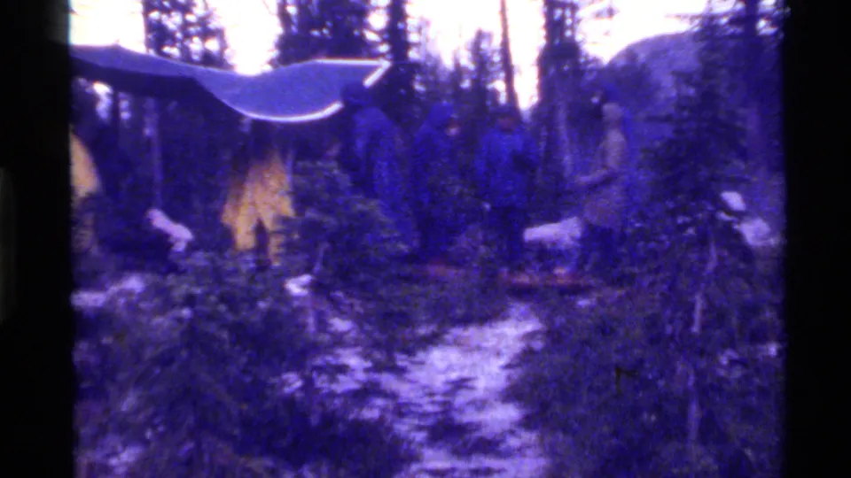 1972 Holland Lake, Montana 8mm frame showing a snowy evergreen forest with a small roofline or wooden structure partly visible.