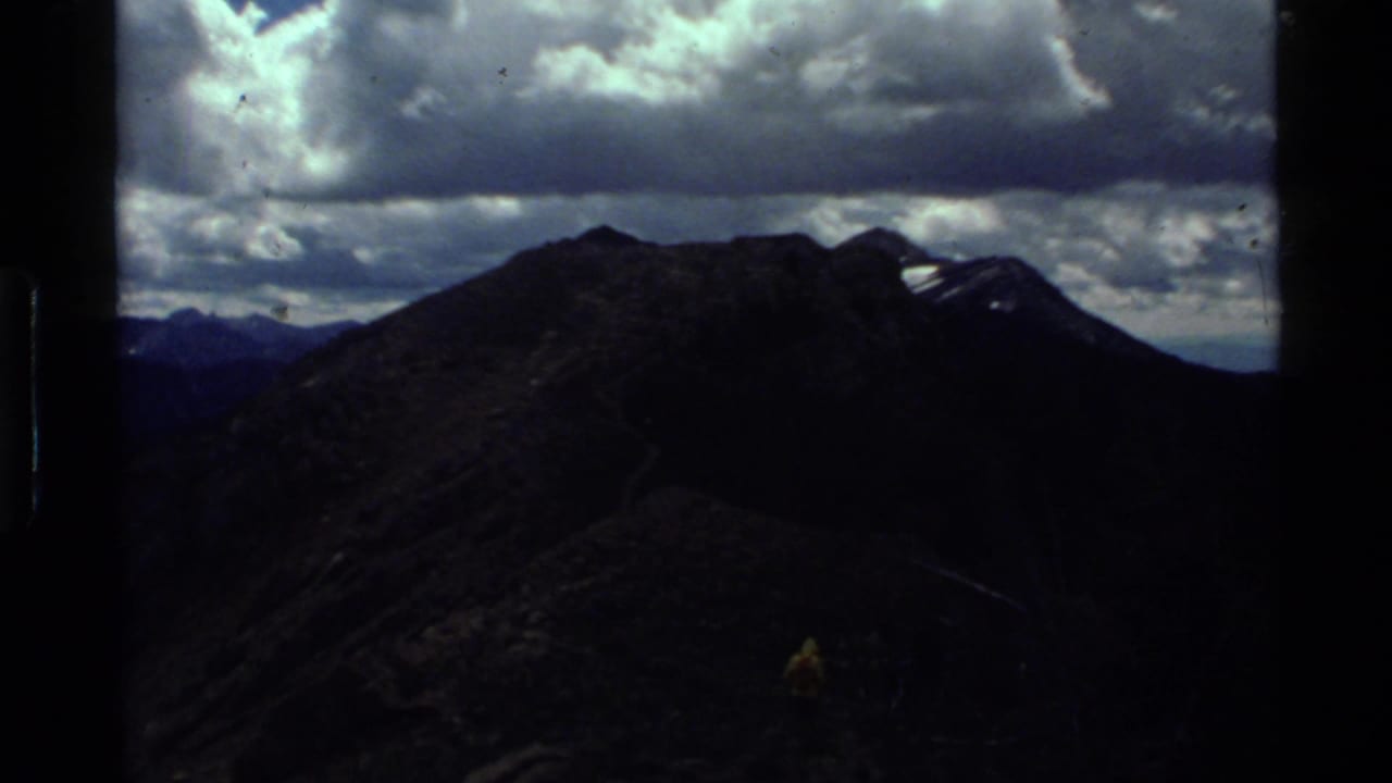 Dark mountain ridge under heavy clouds with a distant hiker on a trail.