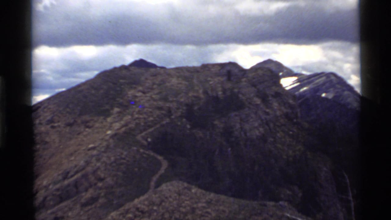 Rocky mountain ridge with a winding trail beneath an overcast sky.