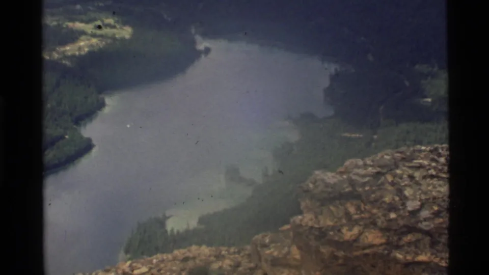 1972 8mm frame of Holland Lake from a high rocky viewpoint, showing winding shorelines and forested peninsulas.