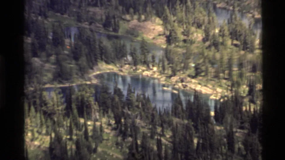 Vintage 8mm view near Holland Lake, Montana, showing a forest-ringed lake basin with reflective water and rocky banks.