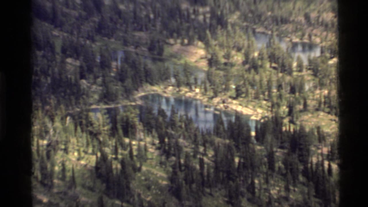 1972 8mm view of the Holland Lake area showing evergreen forest, small lakes, and sloping mountain terrain from above.