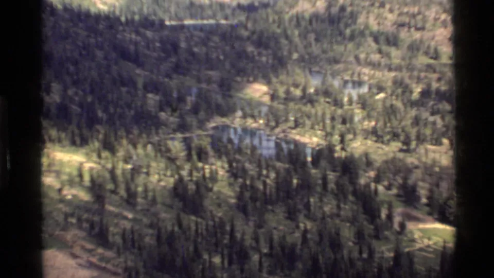 Aerial 8mm frame of the Holland Lake, Montana area with dark trees, small blue water bodies, and rugged terrain.