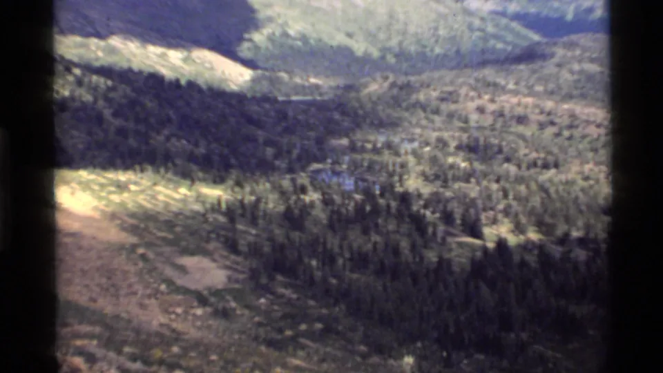 Late-frame 8mm aerial view of the Holland Lake area, showing forest, water, and rugged Montana mountain terrain.