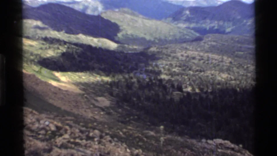 1972 Holland Lake, Montana footage shows a broad valley, evergreen forest, open hillside, and small blue water area below.