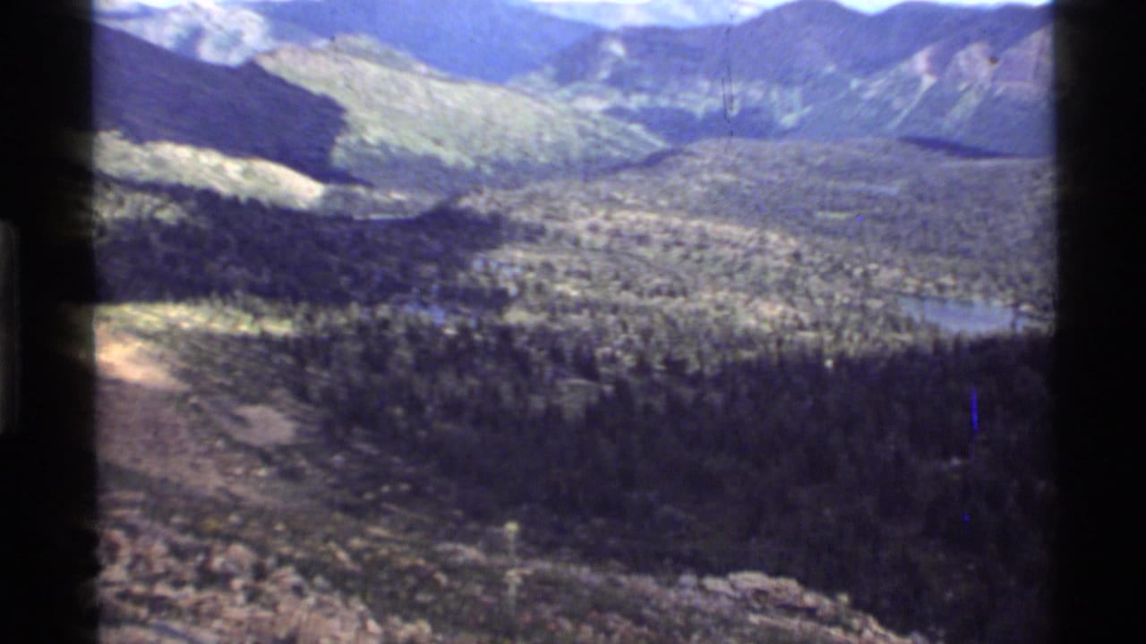 1972 8mm view from above Holland Lake, Montana, showing evergreen forest, a distant lake, and mountain ridges.