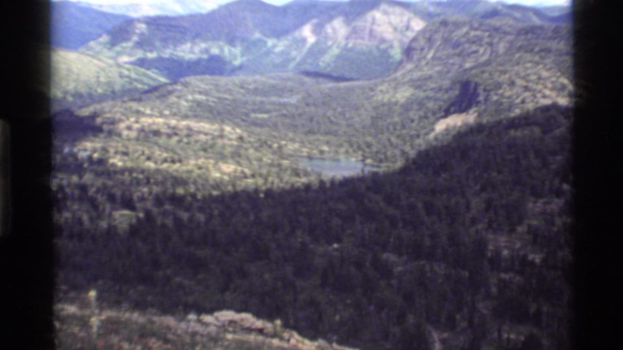 1972 8mm view of Holland Lake, Montana, showing a forested valley, distant lake, and rugged mountain ridges.