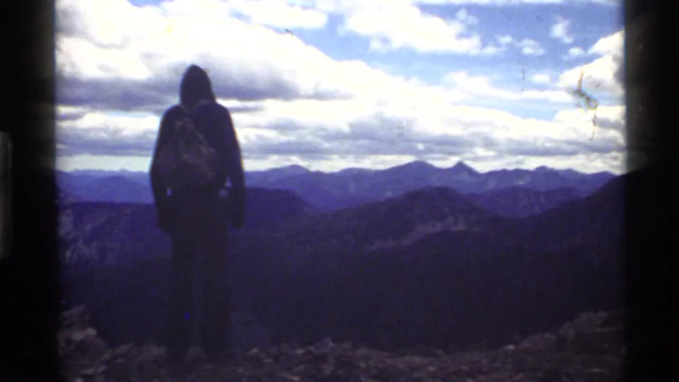Silhouetted backpacker at Holland Lake, Montana, standing before a broad 1972 mountain horizon in 8mm home-movie footage.