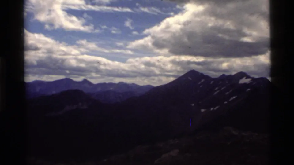Holland Lake, Montana mountain view on 8mm film, with distant peaks, heavy clouds, and dark frame edges.