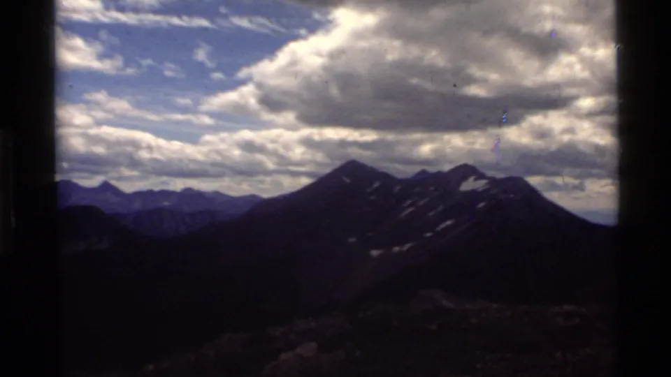 1972 home-movie frame of Montana peaks and a broad cloudy sky near Holland Lake.