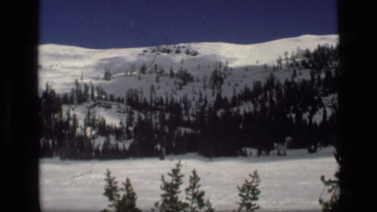 1972 Idaho 8mm view of a snow-covered mountain slope with dark evergreen trees and a deep blue sky.