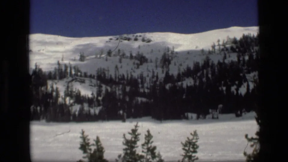 1972 Idaho 8mm view of a snow-covered mountain slope with dark evergreen trees and a deep blue sky.