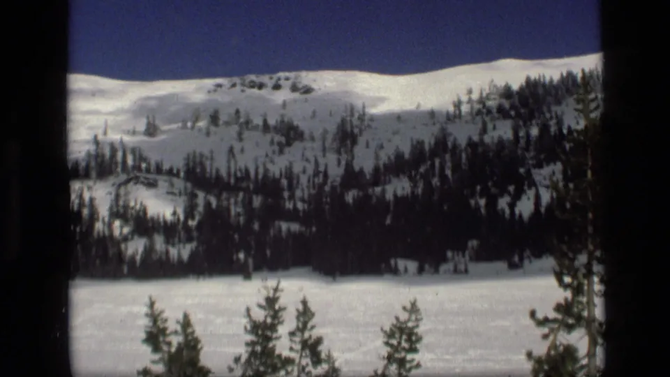A 1972 Idaho winter landscape shows a snowy hillside, scattered evergreens and an open white field in the foreground.