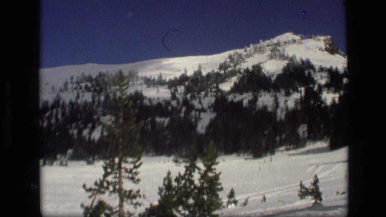1972 Idaho 8mm frame showing a snow-covered ridge, dark pine trees, and blue winter sky within visible film borders.