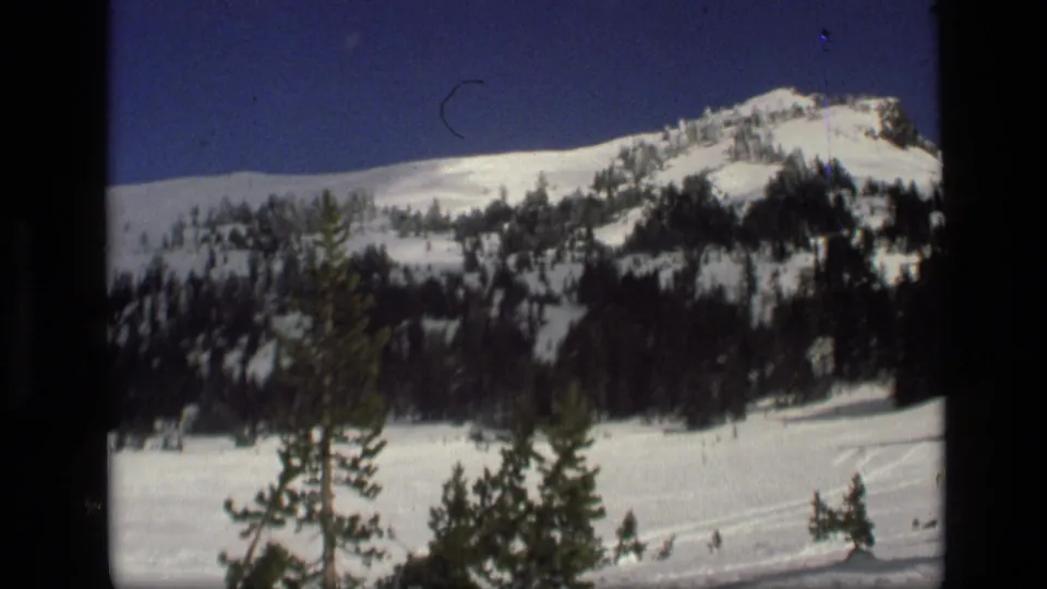 1972 Idaho 8mm frame showing a snow-covered ridge, dark pine trees, and blue winter sky within visible film borders.