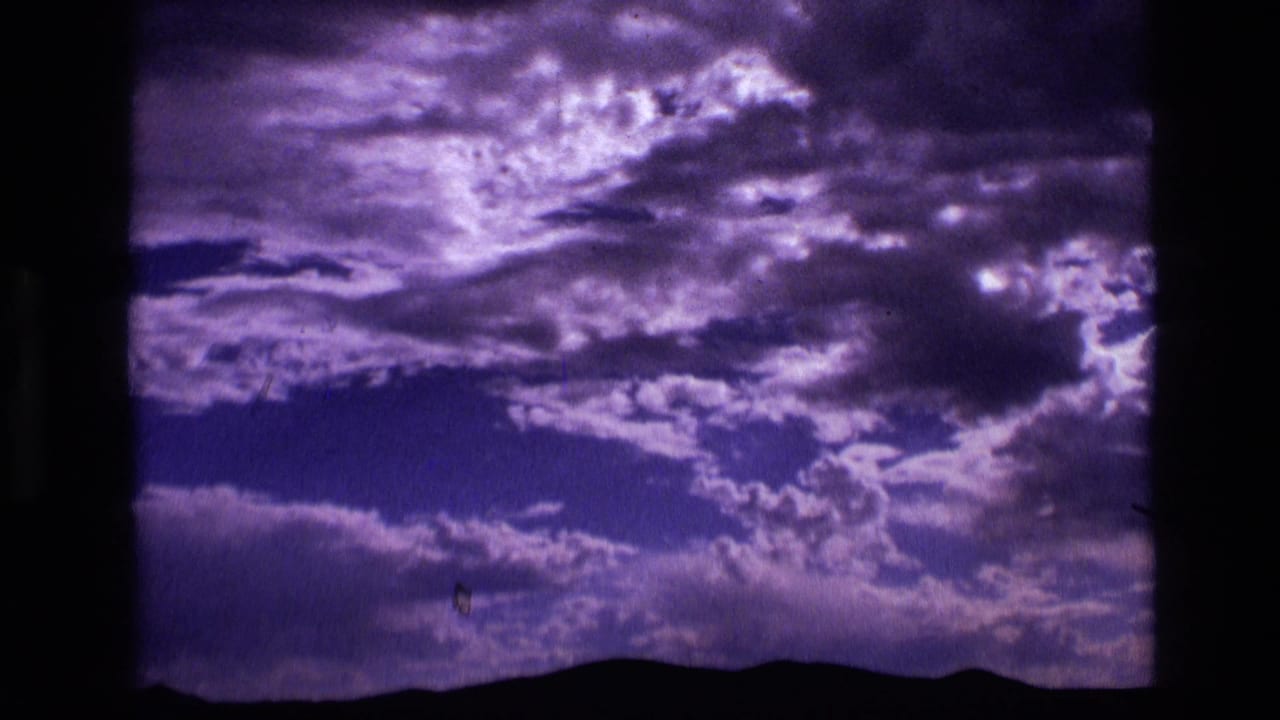 1972 Idaho home-movie frame with illuminated clouds and a dark mountain horizon line.